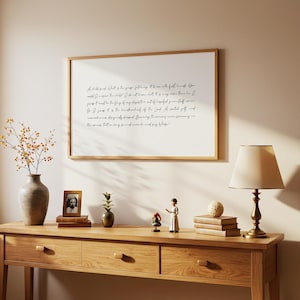 May include: A framed print with handwritten text hangs above a wooden console table. The table displays a vase with branches, a framed photo, a small plant, figurines, books, and a lamp.