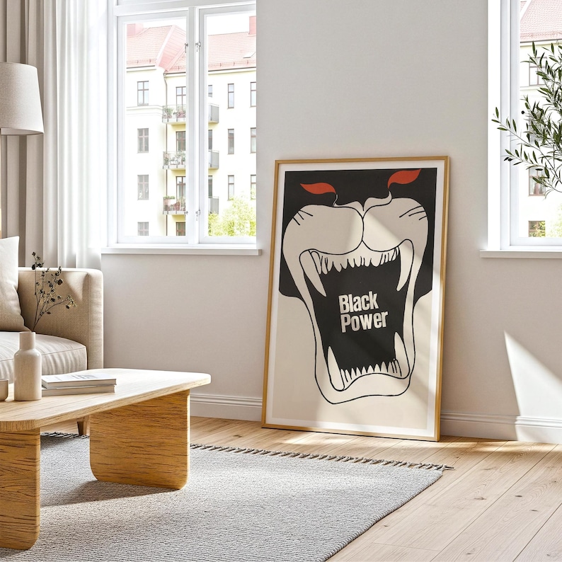 May include: A framed poster with a black panther illustration. The panther's mouth is open, revealing sharp white teeth. The text "Black Power" is in the center. The poster has a gold frame and is leaning against a white wall.