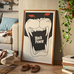 May include: A framed poster with a bold graphic of a roaring black panther head with the words "Black Power" in the center. The poster has a white background with black and red accents, and is displayed in a wooden frame.