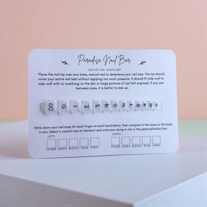 May include: A white card with the text "Paradise Nail Bar" and instructions for instant gel manicures. The card includes a row of numbered nail tip samples and spaces to write down nail sizes for each finger on both hands.