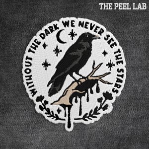 May include: Embroidered patch featuring a black raven perched on a branch, surrounded by a white border with the text "WITHOUT THE DARK WE NEVER SEE THE STARS." The Peel Lab is printed at the top. The design includes a crescent moon and stars.