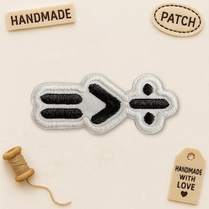May include: Embroidered patch featuring mathematical symbols: equals, greater than, and division. The patch has a white border with black and white details. The word "HANDMADE" is on a wooden tag, and the word "PATCH" is on a stitched oval.