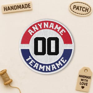 May include: Round embroidered patch with the text "ANYNAME" in red, "TEAMNAME" in blue, and the numbers "00" in black. The patch has a white background and a red and blue border. A small wooden tag says "HANDMADE".