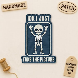May include: Embroidered patch with a skeleton design, arms raised, within a navy blue rectangle. Text reads "IDK I JUST TAKE THE PICTURE". Additional tags say "HANDMADE", "PATCH", and "HANDMADE WITH LOVE".