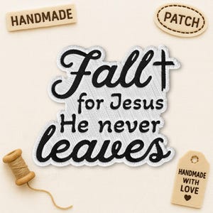 Peut inclure: Écusson brodé avec le texte "Fall for Jesus He never leaves" en écriture noire. L'écusson a un fond blanc avec une texture cousue. Des petites étiquettes supplémentaires indiquent "Handmade" et "Patch". Une bobine de fil est également présente.