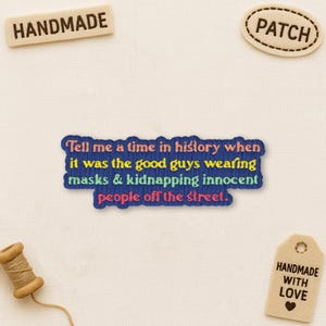 May include: Embroidered blue patch with the text "Tell me a time in history when it was the good guys wearing masks & kidnapping innocent people off the street." Also includes a "HANDMADE" tag and a "PATCH" tag.