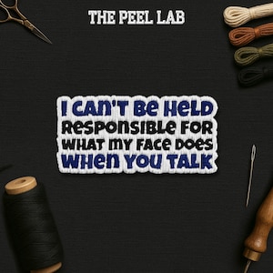 May include: Embroidered patch with the text "I CAN'T BE HELD RESPONSIBLE FOR WHAT MY FACE DOES WHEN YOU TALK" in blue and white. The patch is on a black surface with sewing tools and thread.