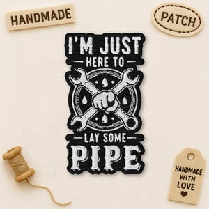 May include: Black patch with white text: "I'M JUST HERE TO - LAY SOME - PIPE" and crossed wrenches. Includes "HANDMADE" and "PATCH" labels, and a "HANDMADE WITH LOVE" tag. A spool of thread is also present.