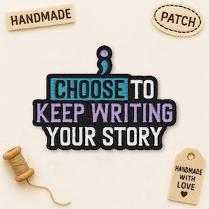 May include: Embroidered patch with the text "CHOOSE TO KEEP WRITING YOUR STORY" in teal, purple, and white. Additional patches and a spool of thread are also visible. The word "HANDMADE" is on a small rectangular patch.