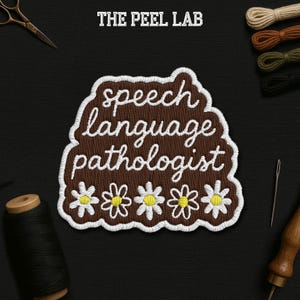 May include: Embroidered patch with the text "speech language pathologist" in white script on a brown background. The patch is bordered with white stitching and features four daisy flowers. The Peel Lab logo is at the top.