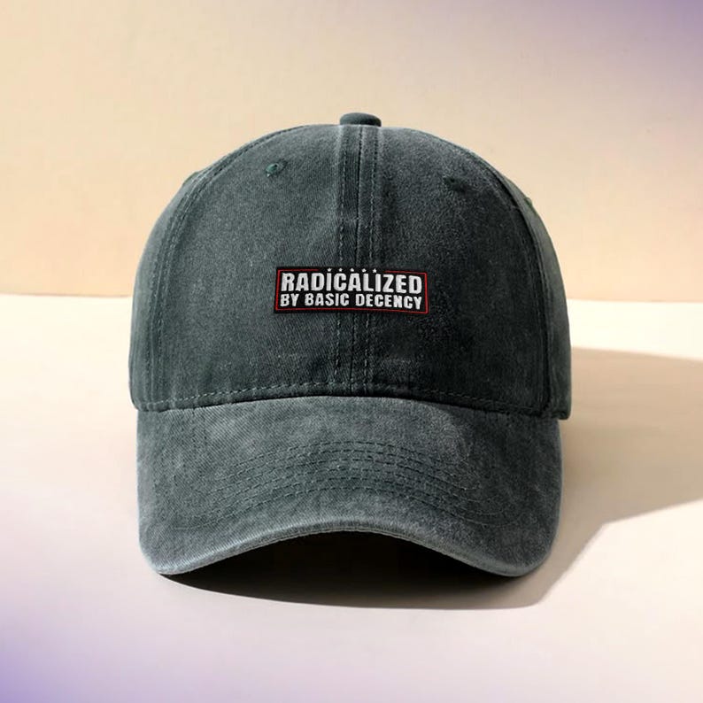 K&ouml;nnte beinhalten: Dunkelgr&uuml;ne Baseballkappe mit gebogenem Schirm. Auf der Kappe befindet sich ein rechteckiger Aufn&auml;her mit dem wei&szlig;en Schriftzug "RADICALIZED BY BASIC DECENCY" auf rotem und schwarzem Hintergrund. Die Kappe ist aus weichem, abgenutztem Material gefertigt.