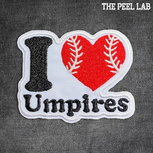 May include: White patch with the words "I Love Umpires" in black lettering. The "Love" is represented by a red heart with white baseball stitching. The patch has a white border.