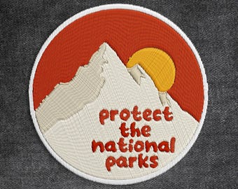 May include: Embroidered patch with a mountain range and a yellow sun set against a red background. The text "protect the national parks" is in red. The Peel Lab is printed at the top.