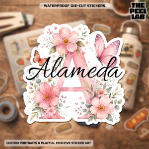 Peut inclure: Un autocollant découpé représentant une grande lettre A rose clair ornée de fleurs roses, de feuilles vertes et de deux papillons de style aquarelle. Le nom Alameda est inscrit au centre dans une police cursive noire et élégante.