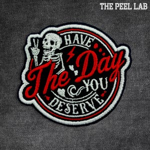 May include: Embroidered patch with a black background, red text, and white accents. The patch features a skeleton giving a peace sign and the phrase "Have The Day You Deserve". The Peel Lab logo is at the top.