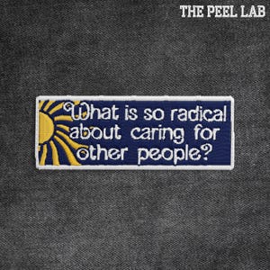May include: Embroidered patch with the text "What is so radical about caring for other people?" in white on a navy blue background. A yellow sun design is on the left. The Peel Lab is printed at the top.