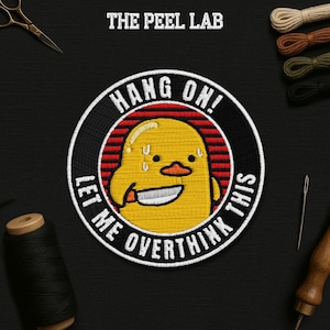 May include: Embroidered patch with a yellow duck character holding a knife, with the text "HANG ON! LET ME OVERTHINK THIS." The patch is circular with a black border and red stripes. The Peel Lab logo is at the top.