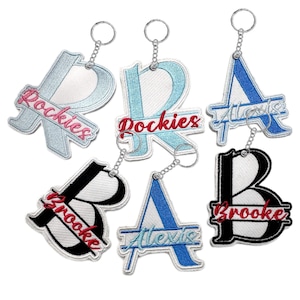 May include: Embroidered keychains in the shape of the letters R, A, and B. The letter R is light blue with the word "Rockies" in red. The letter A is blue with "Alexis" in light blue. The letter B is black with "Brooke" in red.