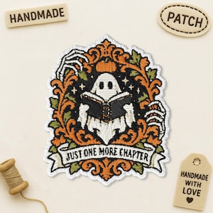 May include: An embroidered patch featuring a white ghost reading a black book, framed by orange and green ornate scrollwork and skeletal hands. A white banner at the bottom displays the black text "JUST ONE MORE CHAPTER" in capital letters.