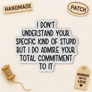 May include: Embroidered patch with the text "I don't understand your specific kind of stupid but I do admire your total commitment to it." Includes a wooden spool of thread, a "handmade" tag, and a "patch" tag.