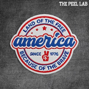 May include: Embroidered patch with a patriotic design. The patch features the word "America" in blue script, surrounded by a red and white border. Text includes "Land of the Free," "Because of the Brave," and "Since 1776."