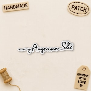 May include: Embroidered patch with the word "Anyname" in a cursive font, followed by two connected hearts. The patch is white with black stitching. Additional patches read "HANDMADE" and "PATCH". A tag reads "HANDMADE WITH LOVE".
