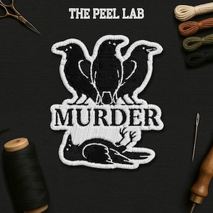May include: Embroidered patch featuring three black crows above the word "MURDER" in white, with a fourth crow below. The text "THE PEEL LAB" is at the top. The patch is on a black background.
