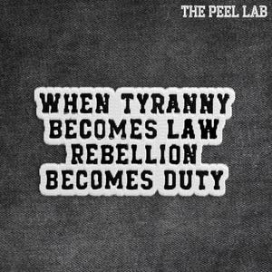 May include: Embroidered patch with the text "WHEN TYRANNY BECOMES LAW REBELLION BECOMES DUTY" in black letters on a white background. The patch is set against a dark gray fabric background. The text "THE PEEL LAB" is at the top.
