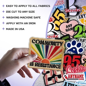 May include: A rectangular patch with the words "COMMUNITY IS RESISTANCE" and a colorful sunburst design. The patch is held by a hand, with other patches visible in the background. The text "EASY TO APPLY TO ALL FABRICS" is also visible.