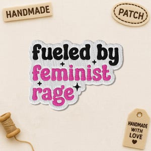 May include: Embroidered patch with the text "fueled by feminist rage" in black and pink. The patch is white with a black border and small black star accents. Additional tags read "handmade", "patch", and "handmade with love".