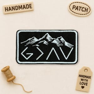 May include: A black embroidered patch with a mountain range design and the letters G > A V in white. The patch is rectangular with a black border. Additional tags read "HANDMADE", "PATCH", and "HANDMADE WITH LOVE".