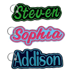 May include: Three personalized name keychains. The top keychain says "Steven" in green lettering on a black background. The middle keychain says "Sophia" in pink lettering on a light blue background. The bottom keychain says "Addison" in light blue lettering on a navy blue background.