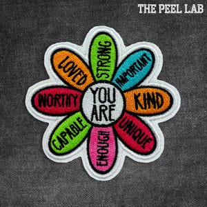 May include: Embroidered flower patch with the words "YOU ARE" in the center, surrounded by colorful petals with positive affirmations like "WORTHY," "STRONG," and "UNIQUE." The patch has a white border and is set against a dark gray background.