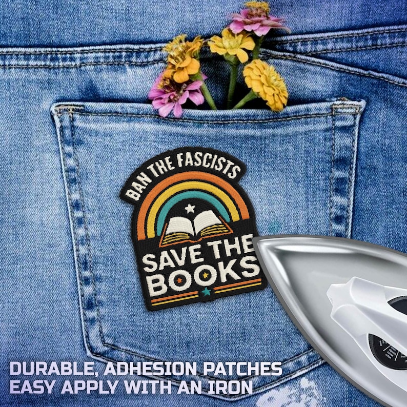 May include: A black and colorful patch with the text "BAN THE FASCISTS" and "SAVE THE BOOKS" is placed on a blue denim pocket. The patch features a rainbow and an open book design. A few colorful flowers are in the pocket. An iron is in the image.