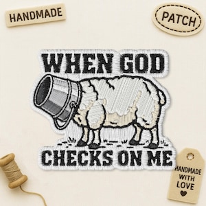 May include: An embroidered patch featuring a white sheep with a grey bucket over its head. The text reads WHEN GOD CHECKS ON ME in black block letters above and below the sheep. The patch has a white border and is set against a light fabric.