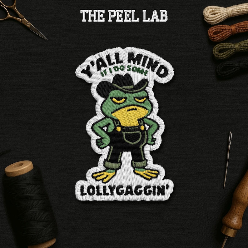 May include: Embroidered patch with a grumpy green frog in a cowboy hat and dungarees. Text reads "Y'all mind if I do some lollygaggin'?" in white thread. The Peel Lab logo is at the top. The patch is on a black background.