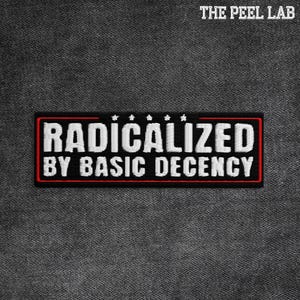 May include: Embroidered patch with the text "RADICALIZED BY BASIC DECENCY" in white, outlined in red, on a black rectangular background. The patch has a red border and is set against a textured gray fabric.