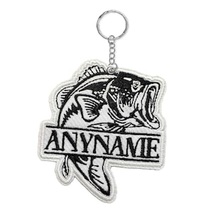 May include: Embroidered keychain featuring a black and white bass fish design with the text "ANYNAME" on a banner. The keychain has a silver-colored metal ring and chain.