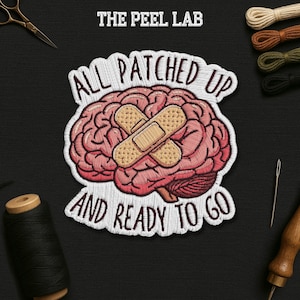 May include: Embroidered patch featuring a pink brain with two bandages, the text "ALL PATCHED UP AND READY TO GO" in white, and the text "THE PEEL LAB" at the top. The patch is surrounded by sewing supplies on a black surface.
