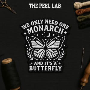 May include: Embroidered black and white patch with the text "WE ONLY NEED ONE MONARCH AND IT'S A BUTTERFLY". The patch features a butterfly design with a crescent moon and stars. The Peel Lab logo is at the top.