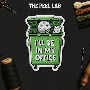 May include: Embroidered patch featuring a cartoon opossum in a green trash can, with the text "I'll Be In My Office." The patch has a white border and the text "THE PEEL LAB" at the top. The opossum is holding a clipboard.