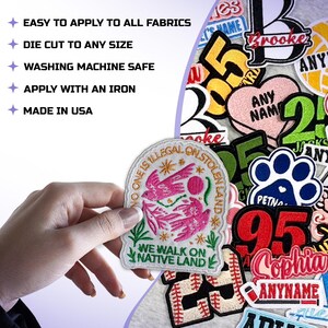 May include: Embroidered patch with the text "NO ONE IS ILLEGAL ON STOLEN LAND" and "WE WALK ON NATIVE LAND". The patch features pink birds and floral designs. The image also shows other patches with various designs and text.
