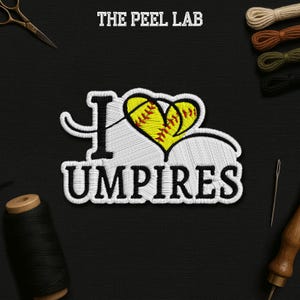 May include: Embroidered patch with the text "I Umpire" in white thread. The "I" is stylized, and the heart is a yellow softball with red stitching. The Peel Lab is printed at the top. The patch is on a black background.