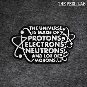 May include: Black and white embroidered patch with the text "THE UNIVERSE IS MADE OF PROTONS ELECTRONS NEUTRONS AND LOT OF MORONS." The patch has a black background with white text and a white border. The Peel Lab logo is at the top.