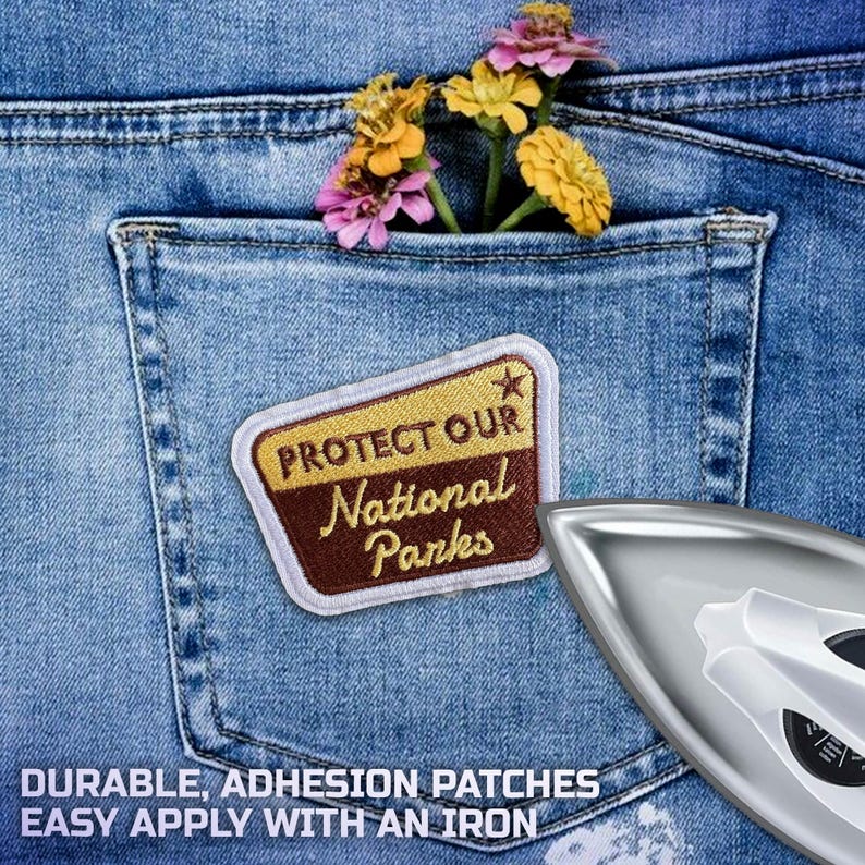 May include: A denim pocket holds colorful flowers and a patch that reads "PROTECT OUR National Parks." The patch is brown and gold with a white border. An iron is in the lower right corner. The text at the bottom says "DURABLE, ADHESION PATCHES EASY APPLY WITH AN IRON."