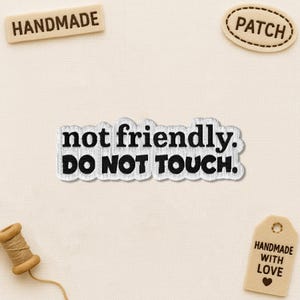 May include: A collection of handmade patches and tags. The central patch reads "not friendly. DO NOT TOUCH." Other tags say "HANDMADE," "PATCH," and "HANDMADE WITH LOVE."