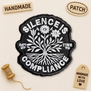 May include: A black embroidered patch with white text that reads "SILENCE IS COMPLIANCE" around a tree design. The patch also has the words "ACT UP" and "TIME TO". There are two small wooden tags that say "HANDMADE" and "HANDMADE WITH LOVE".