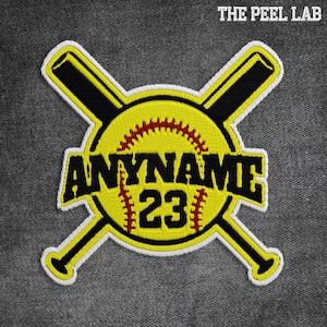 May include: Embroidered patch with a yellow softball design, red stitching, crossed black bats, and the text "ANYNAME 23". The patch has a white border and the text "THE PEEL LAB" at the top.