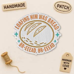 May include: Embroidered patch with the text "LOAFING HIM WAS BREAD" in orange, featuring bread loaf illustrations. The patch is white with an orange border and teal accents. Includes "HANDMADE" and "PATCH" labels.