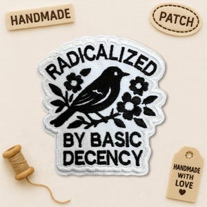 May include: Embroidered patch with a black bird perched on a floral branch, with the words "RADICALIZED BY BASIC DECENCY" in white. The patch is surrounded by a white border. Additional tags read "HANDMADE" and "PATCH".